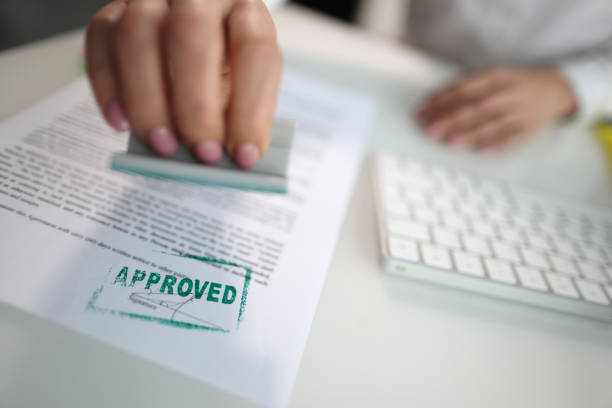 Closeup of a person hand stamping green approved seal on text approved document on table Closeup of a person hand stamping green approved seal on text approved document on table. Contract form and business agreement with partner representing stock pictures, royalty-free photos & images