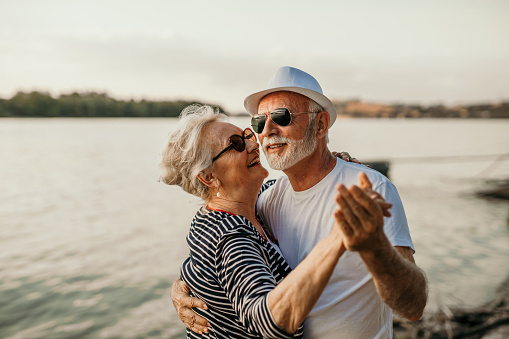 Beach dance, senior couple and smiling man and woman standing in sea or lake or river water and hugging at sunset. Happy, smiling for a marriage anniversary or love while dancing in nature with trust.