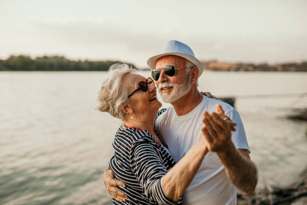 Dance with me Beach dance, senior couple and smiling man and woman standing in sea or lake or river water and hugging at sunset. Happy, smiling for a marriage anniversary or love while dancing in nature with trust. habitat 67 stock pictures, royalty-free photos & images