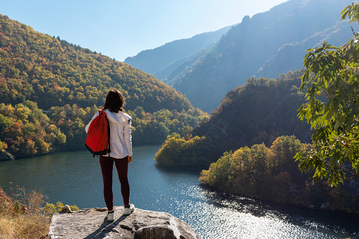 Woman traveler with backpack relaxing enjoying beautiful view of peaceful place of mountain river in Rhodopes mountains, Balkans, Bulgaria, Europe. Travel, walking, hiking, active lifestyle