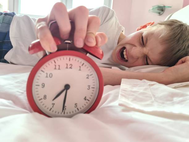 Stressed tired boy sleeping in bed with an alarm clock Stressed tired boy sleeping in bed with an alarm clock. Morning and time to get up laziness aggression emotions school alarm stock pictures, royalty-free photos & images