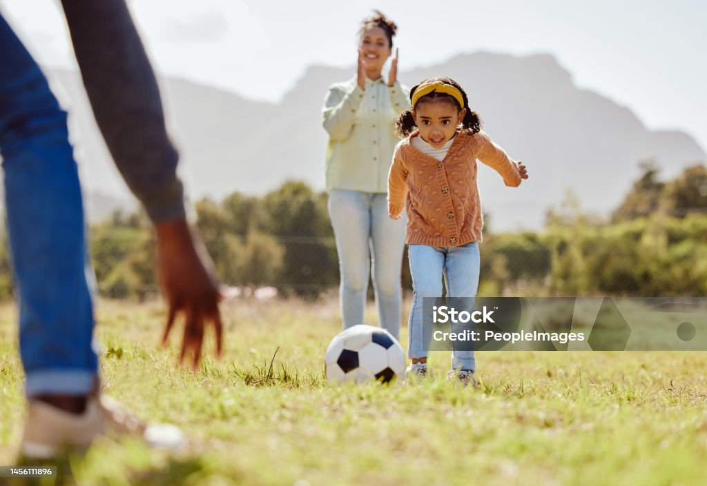 Parents, park and girl kick soccer ball for fun sports learning, bonding and relax in sunshine, garden and nature together. Happy family, little girl and black people playing football on grass field 25-29 Years Stock Photo