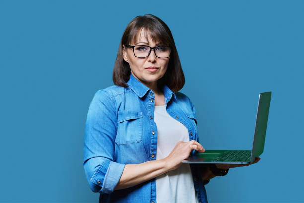 istock Serious mature woman using laptop on blue background 1456111936
