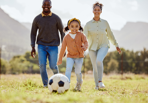 Happy family, soccer ball and playing on the grass in nature for fun, bonding and active exercise in the outdoors. Mother, father and child enjoying quality family time together with ball on a field