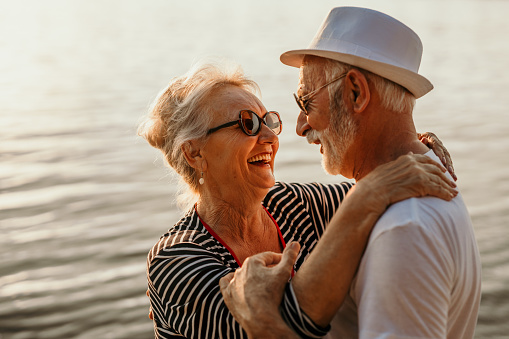 Happy Caucasian family on a beach vacation. Smiling senior couple holding hands and dancing on tropical beach at summer sunset. Healthy elderly retired man and woman relax and enjoy a romantic holiday together