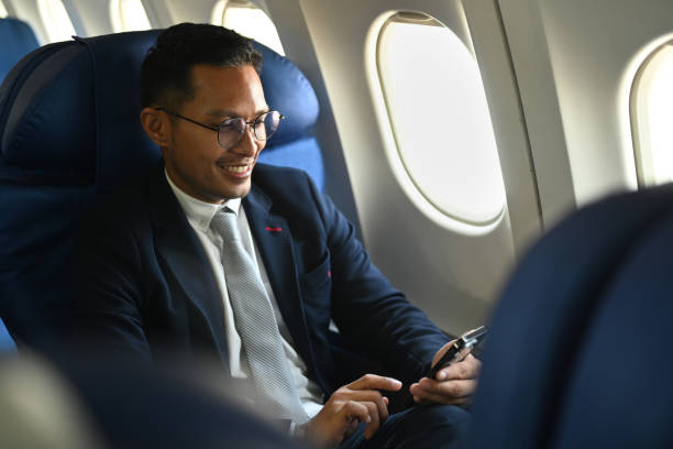 istock Positive businessman in formal clothes using mobile phone while sitting in airplane cabin near window. 1456114190