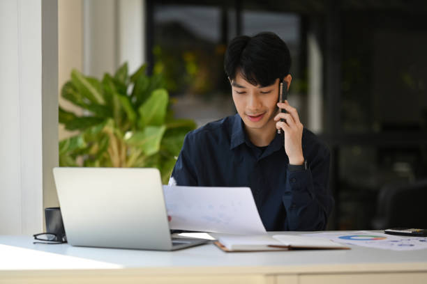 istock Handsome male financial advisor looking at document and talking on mobile phone with client. 1456114290