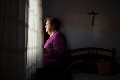 Portrait of old lady standing beside window in bedroom