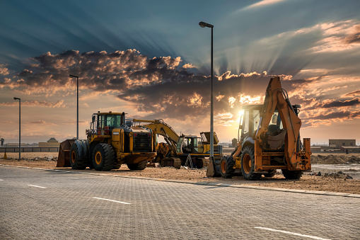 a few earthmoving machines parked on the site at sunset