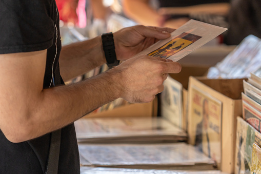 Selective focus on the right hand of an unrecognizable man at a flea market looking for vinyl records.