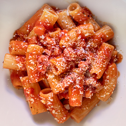 A closeup of a dish with Italian pasta with tomato sauce, bacon, and parmesan on top