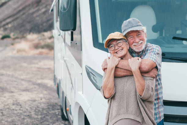 Beautiful senior couple on leisure travel embracing affectionately while standing outside their motorhome. Mature couple enjoying freedom and retirement with an alternative life in motorhome Beautiful senior couple on leisure travel embracing affectionately while standing outside their motorhome. Mature couple enjoying freedom and retirement with an alternative life in motorhome rv travel stock pictures, royalty-free photos & images