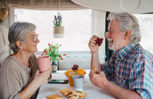 Beautiful caucasian senior couple in travel vacation leisure inside a camper van dinette enjoying breakfast together. Happy retired and free lifestyle