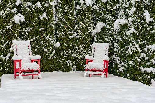 Two red lawn chairs covered in snow on a patio