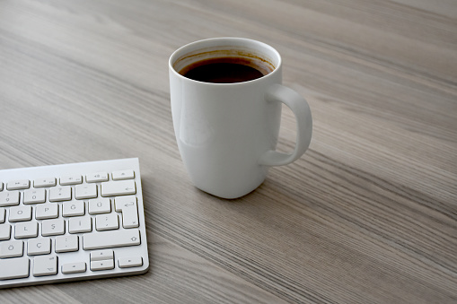 Cup of coffee on the wood table with computer keyboard and copy space