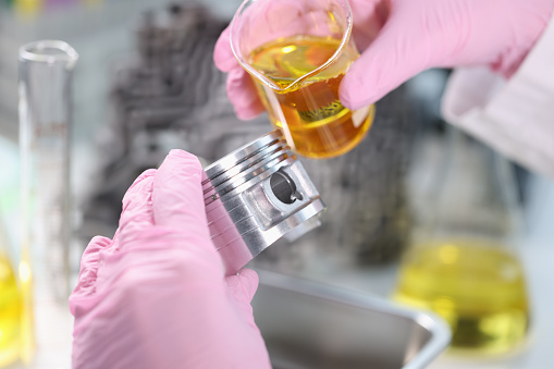 Scientist pours engine oil on piston of car in laboratory closeup. Lubrication and testing of car parts concept