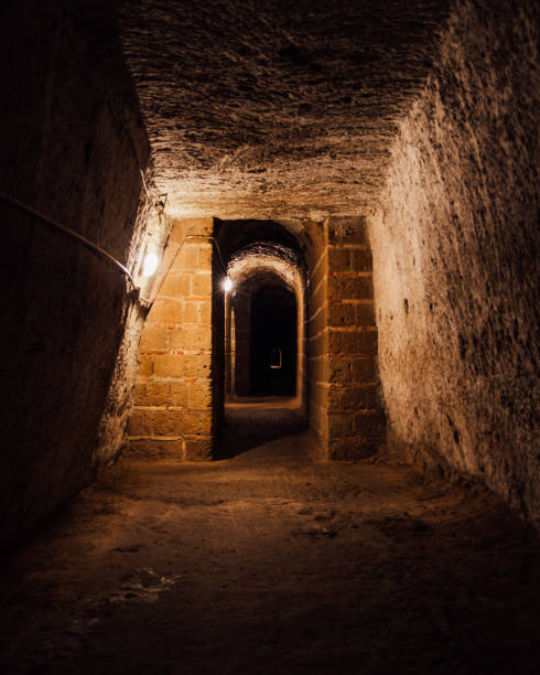 vista di una sala vuota con ingressi ad arco e muri in pietra in una catacomba o città sotterranea - catacomb foto e immagini stock