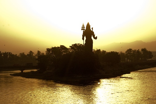 Haridwar, India – October 02, 2013: Lord Shiva statue overlooking Haridwar holy town in India at golden sunrise.Located in foothills of Himalayan mountains on bank of Holy Ganges river.