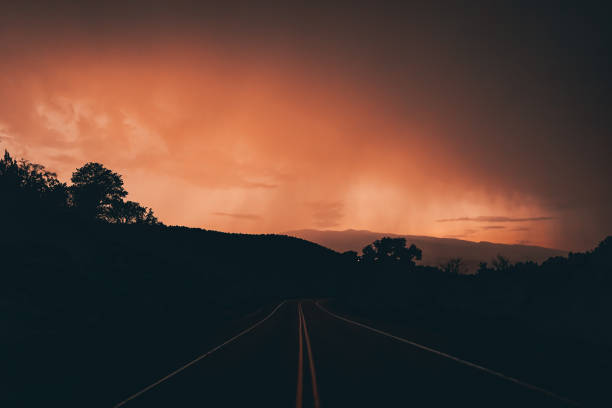 An empty road with yellow indicator lines with an orange sunset sky in the horizon