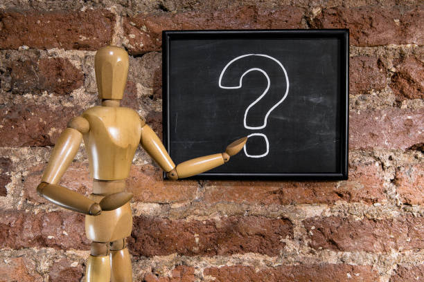 A wooden mannequin showing a question mark on chalkboard, blackboard over a brick wall background
