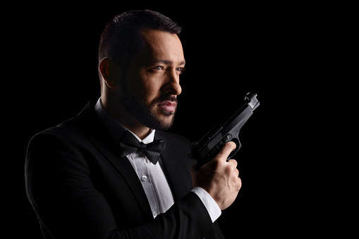 Man with a bow tie holding a gun isolated over black background