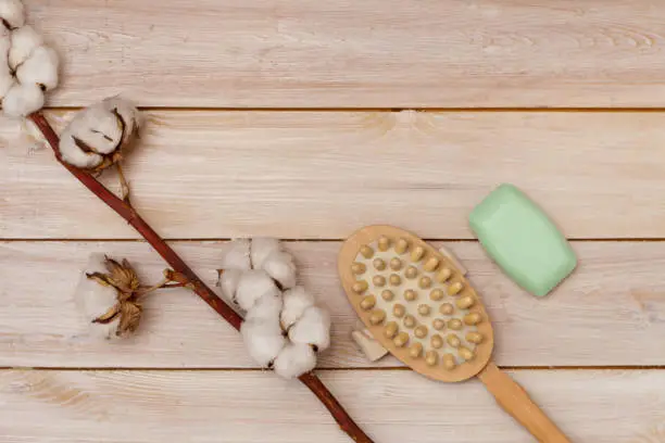 massage brush and soap bar on light wooden table, cotton flower closeup. sponge for bath