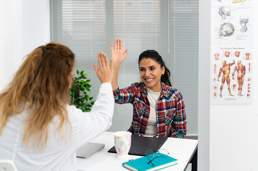 Young women patient giving high five to female doctor at medical office