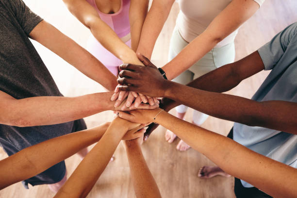 Top view of a group of multicultural people putting their hands together in a huddle before yoga. Group of sporty young people starting a yoga class in a community fitness studio.