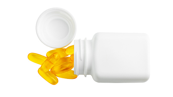 Yellow capsules of omega-3 with bottle, fatty acid pills, nutritional supplement, isolated on white background, top view.