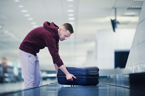 Traveling by airplane. Passenger pick up his blue suitcase in baggage claim in airport terminal.