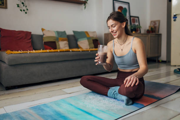 istock Smiling woman drinks a milkshake while sitting on an exercise mat in the living room 1456162302