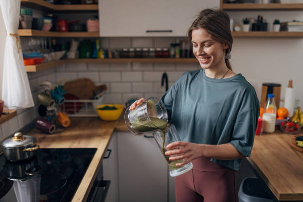 smiling woman pours freshly made smoothie from blender into drinking glass - blender apple banana color image imagens e fotografias de stock