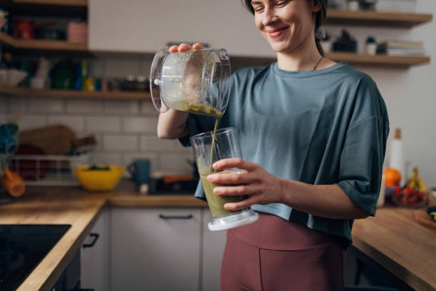 fit woman pours freshly made smoothie from blender into drinking glass - blender apple banana color image imagens e fotografias de stock