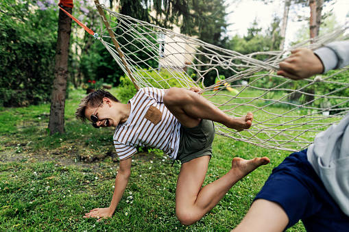 Teenage boys playing on hammock on a spring day. They are swinging, fighting and pushing each other from the hammock.\nCanon R5