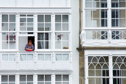 Viveiro, Spain_ August 13, 2010: Galería, traditional glass facade close-up, senior woman looking through window. Viveiro, A Mariña, Lugo province, Galicia, Spain