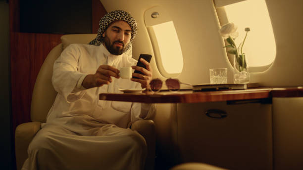istock Happy man looking cellphone in private jet. Smiling arabian rest drinking coffee 1456165643