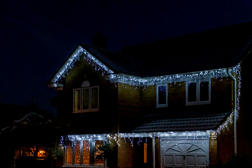 Night image of Christmas lights outside houses on Stukeley Meadows estate, Huntingdon, Cambridgeshire, England, UK.  there is snow on the ground and streetlights are on.