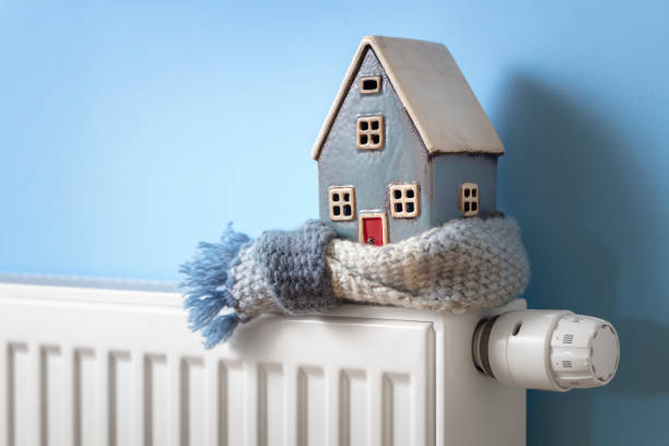 House model wrapped in scarf on radiator winter energy, heating and insulation background stock photo