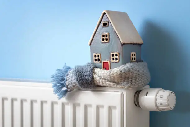 Photo of House model wrapped in scarf on radiator winter energy, heating and insulation background