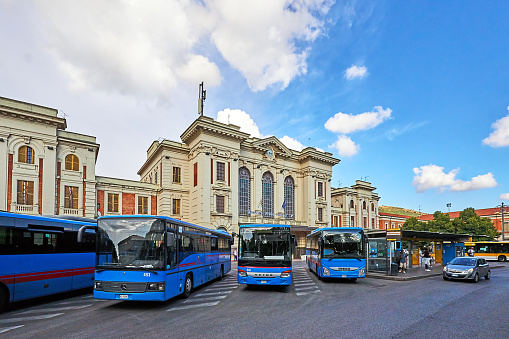 Prato, Italy - September 03, 2022: Pedestrians in front of the train station in Prato near Florence. Blue public transport buses in the foreground.