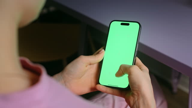 Young woman sitting on armchair at home and uses smartphone with green screen Mock-up. scrolling motion 4k