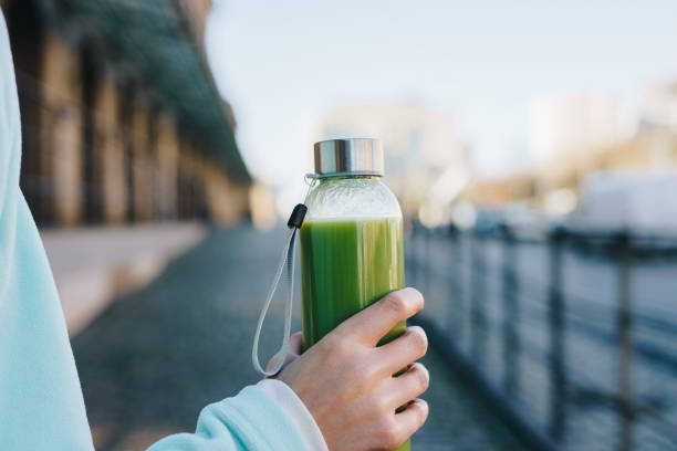 Close up of a woman holding a glass  bottle with green healthy smoothie