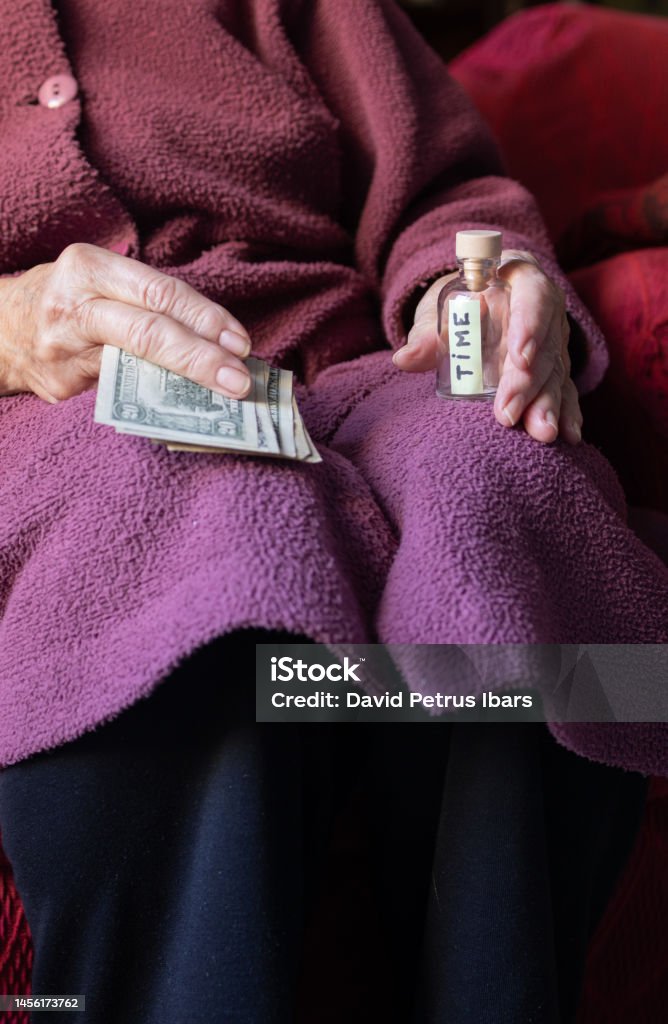 old woman's hand with money bills and a bottle with the word time inside. concept of finite time and priceless value. selling the time of life. 80-89 Years Stock Photo