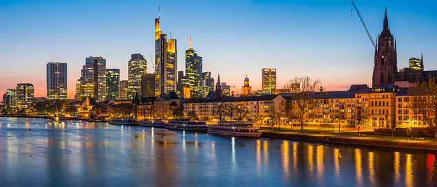 The glittering skyscrapers of Frankfurt’s Bankenviertel finance district illuminated at sunset above the bridges of the River Main in the heart of Germany’s vibrant second city.
