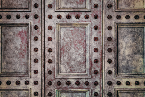 Detail of an ancient paneled door, with painted surface and decorative studs. Vintage background image with space for text.