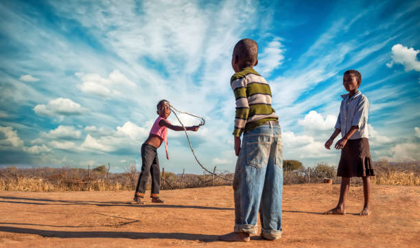tres amigos africanos saltando la cuerda en el pueblo - africa child village smiling fotografías e imágenes de stock