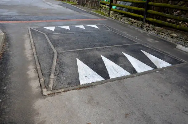 in the middle of the road leading to the residential area, the police and the traffic office installed a red plastic retarder. raised square made of rubber beveled on the sides, arrow, triagle, roadway, speed-bump