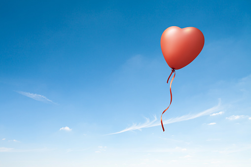 Heart shaped red balloon on blue sky. This file is cleaned and retouched.