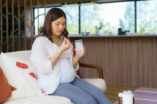 Asian woman pregnant mother holding medicine supplement drugs and glass of water - taking vitamins during pregnancy stock photo