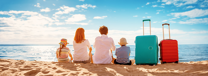 Mother and father with their children sitting on the beach with suitcases. Concept of the family vacation and tourism.